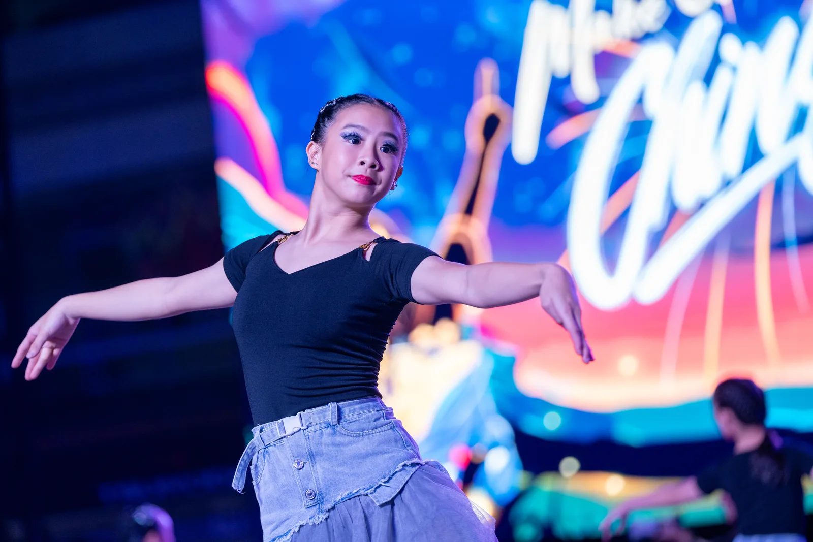 Strongest brand-fit frame in the set: dancer mid-move under dramatic stage light against a deep blue backdrop, clean subject separation and