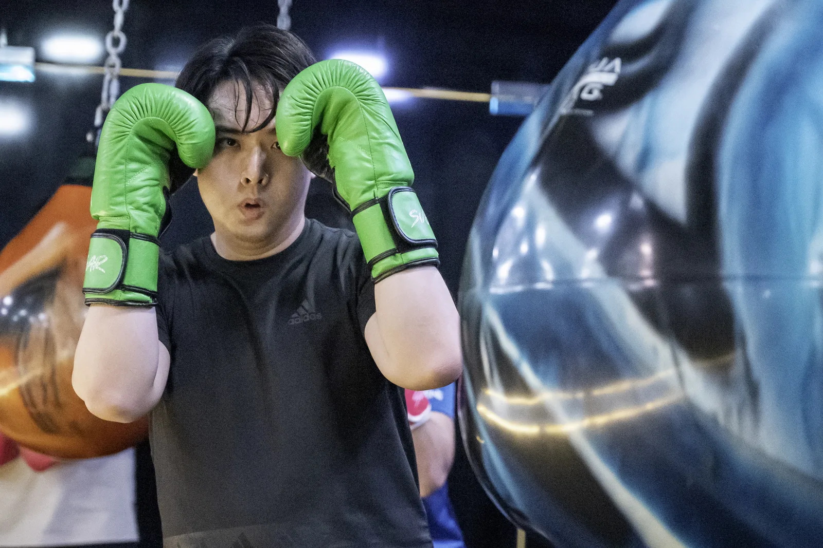 Cinematic low-key sports frame — boxer guarding up behind a motion-blurred bag, moody light and tight crop