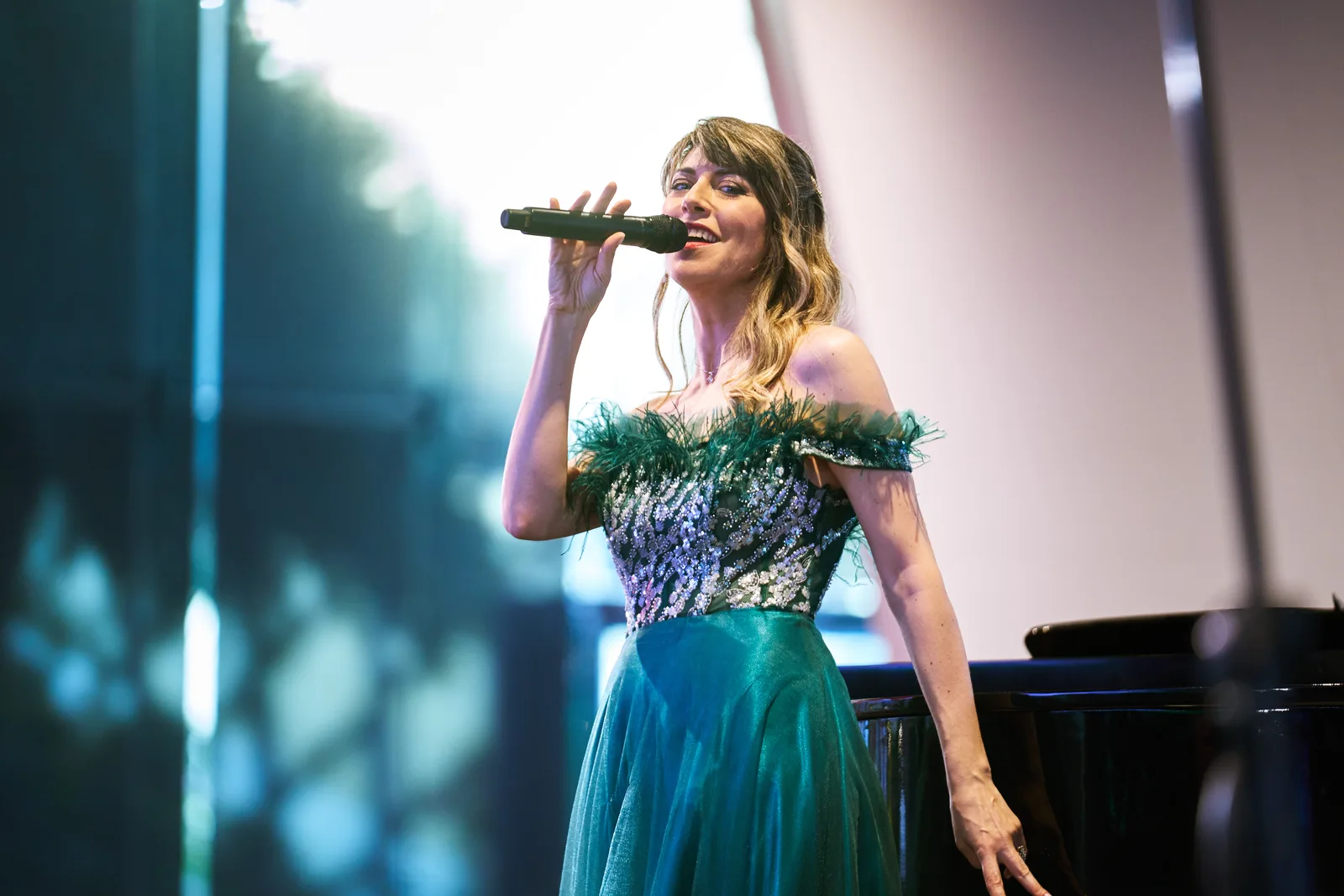 Singer in green sequined gown at the piano, dappled stage light, elegant colour