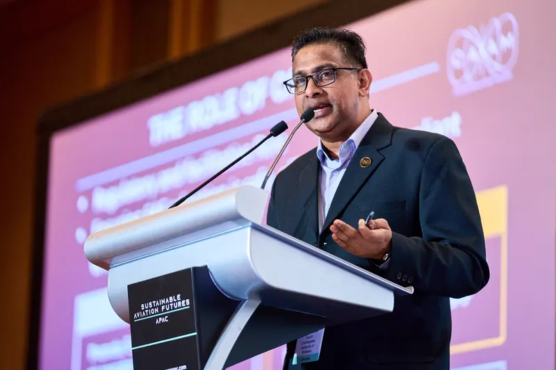 Speaker delivering a keynote from a podium beside a presentation screen at a Singapore conference