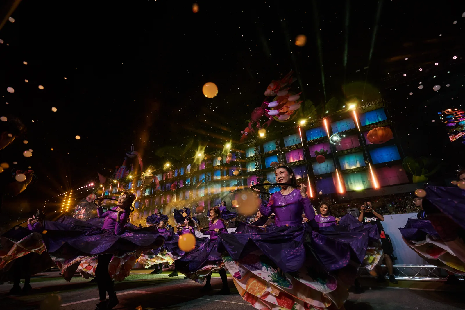 Night performance — dancers in purple against a colourful light wall with foreground bokeh