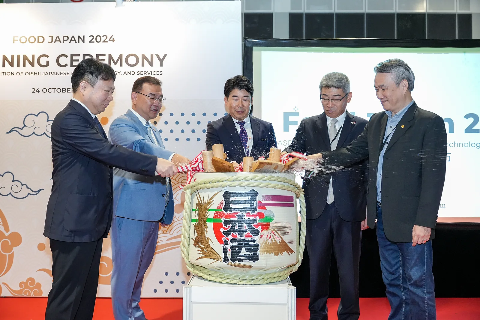 FOOD JAPAN 2024 kagami-biraki caught mid-splash with dignitaries lined across the branded stage — real peak-moment timing at a corporate ope