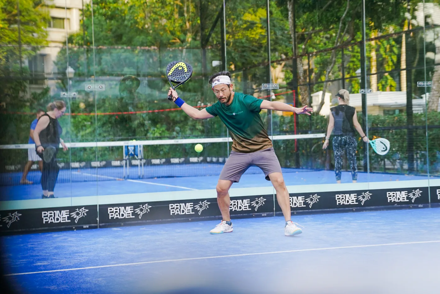 Padel player at full stretch with ball frozen in frame — excellent action timing and clean court geometry