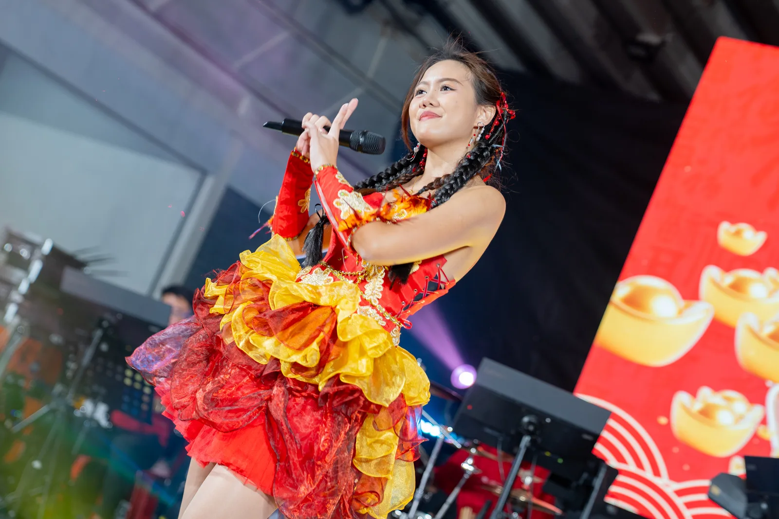 Stage singer in red/orange dress under stage light, dynamic pose against CNY backdrop — closest frame to the brand's dramatic-stage-light ae