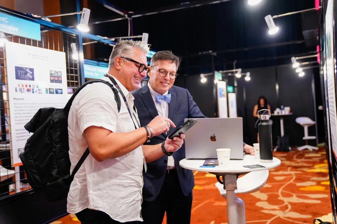 Two visitors looking at a laptop, water bottle and branded cups displayed on a table at a Singapore exhibition booth