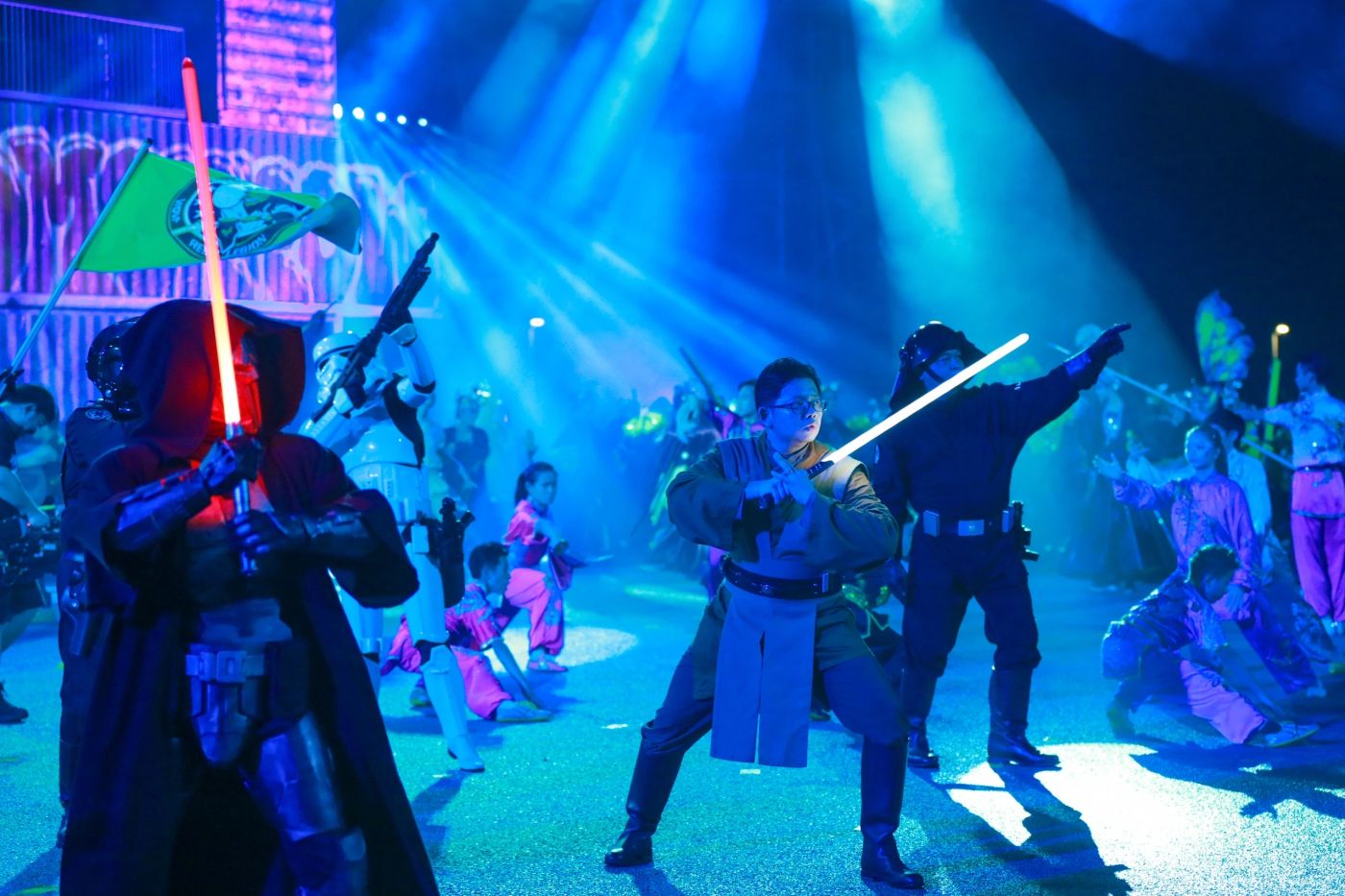 Costumed performers duelling with lightsabers under blue light