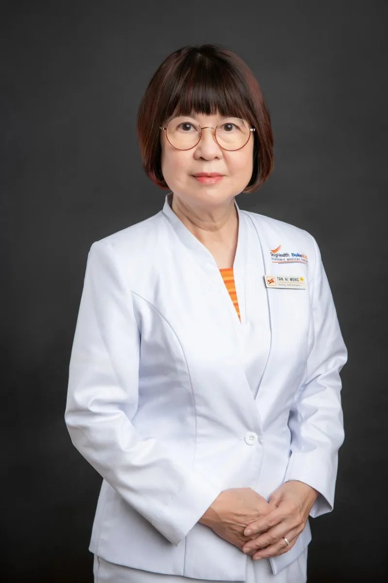 Studio-style headshot of a hospital nursing administrator in uniform against a grey backdrop, name badge visible