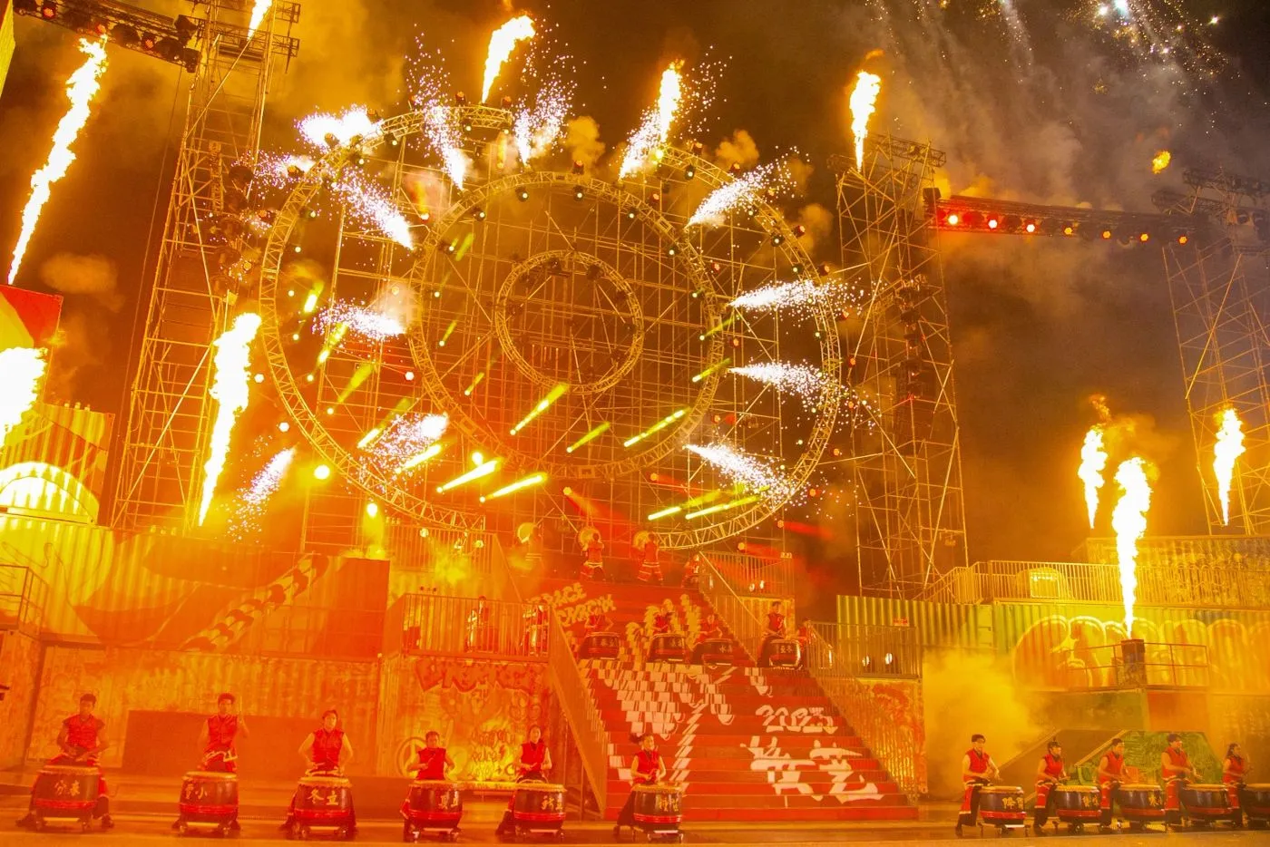 Pyrotechnic wheel and flames over a festival stage at night