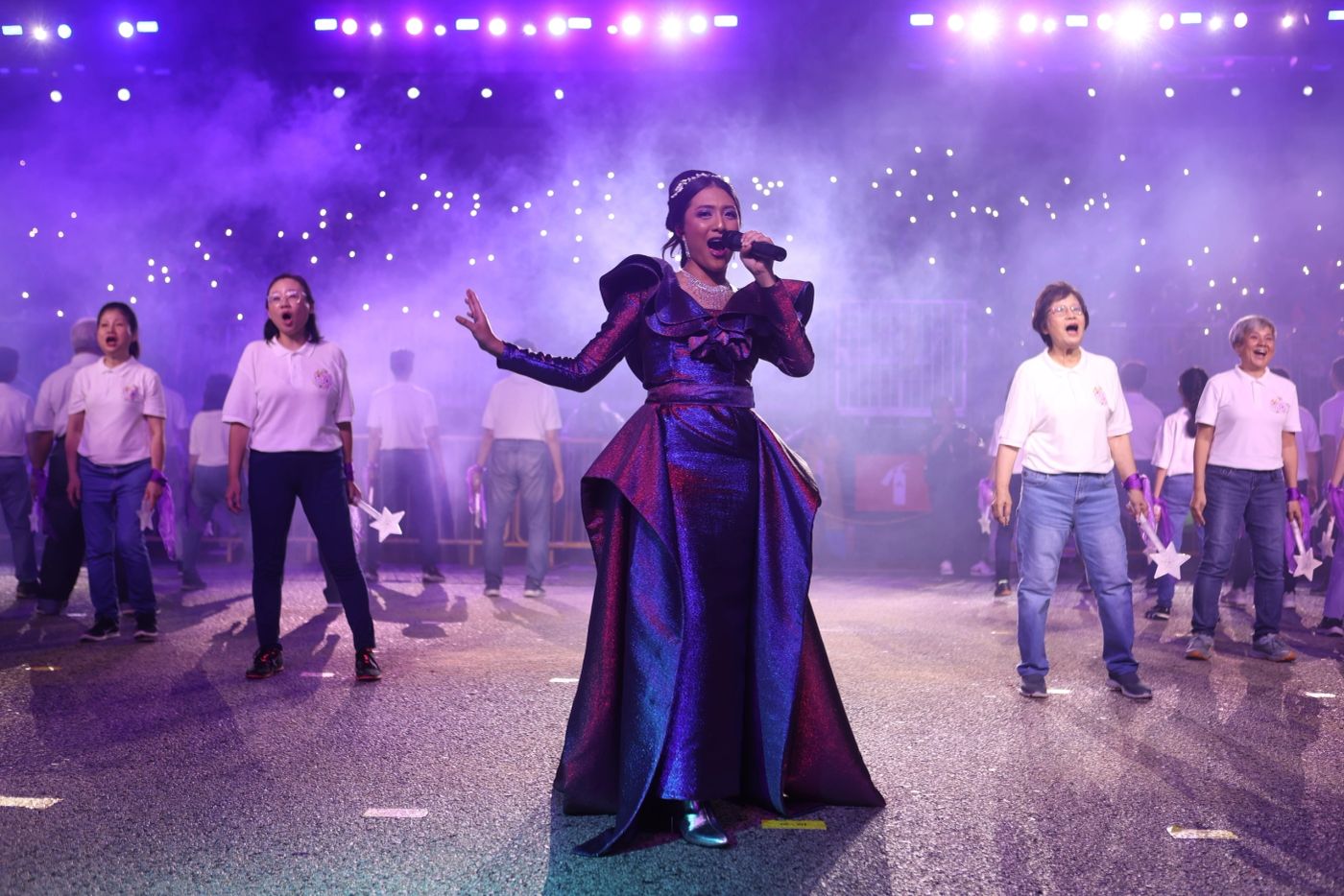 Singer in a flowing gown performing on a national stage with choir