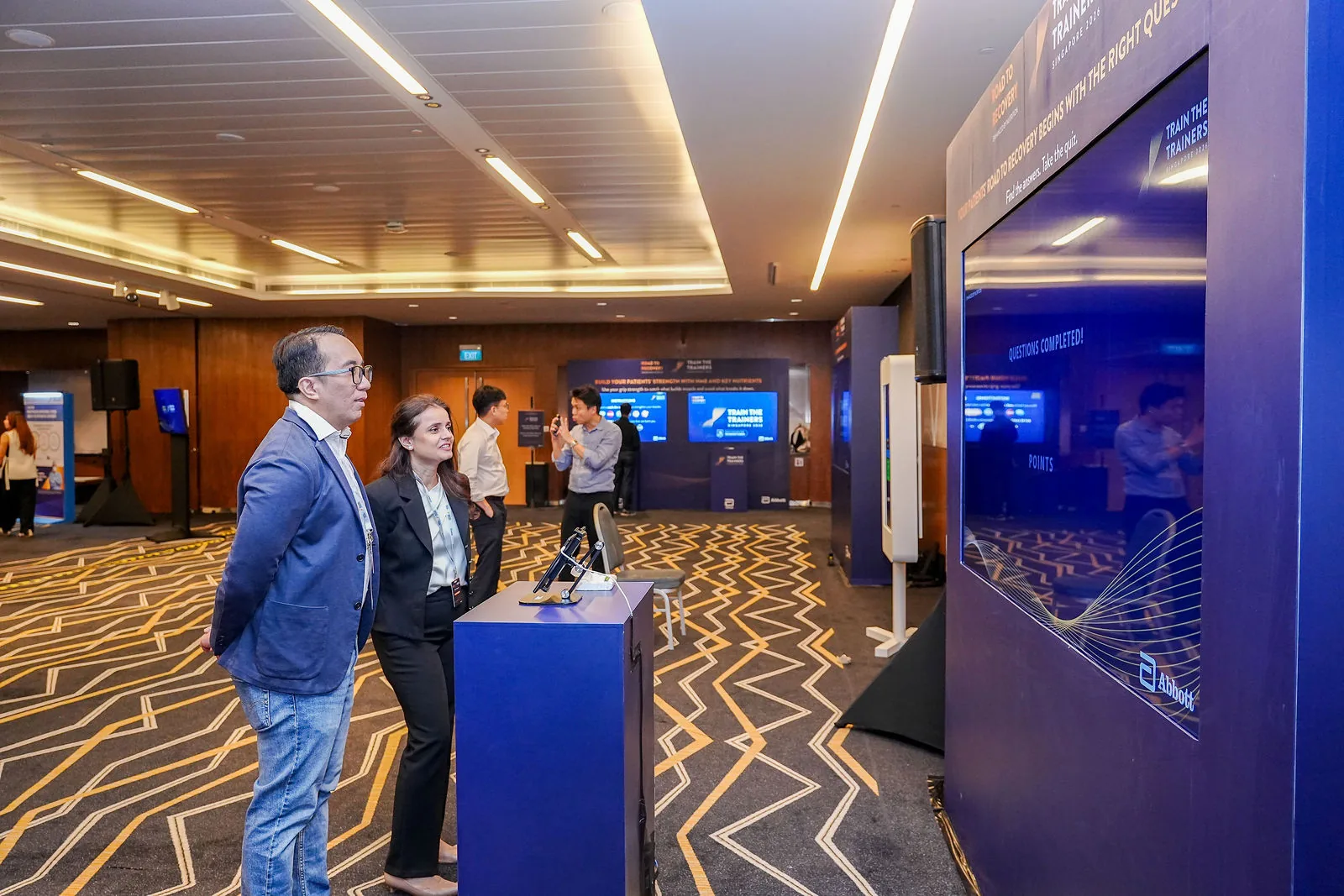 Delegates in a Suntec Singapore concourse during a conference, with the venue's patterned carpet and wood panelling — RS Photography